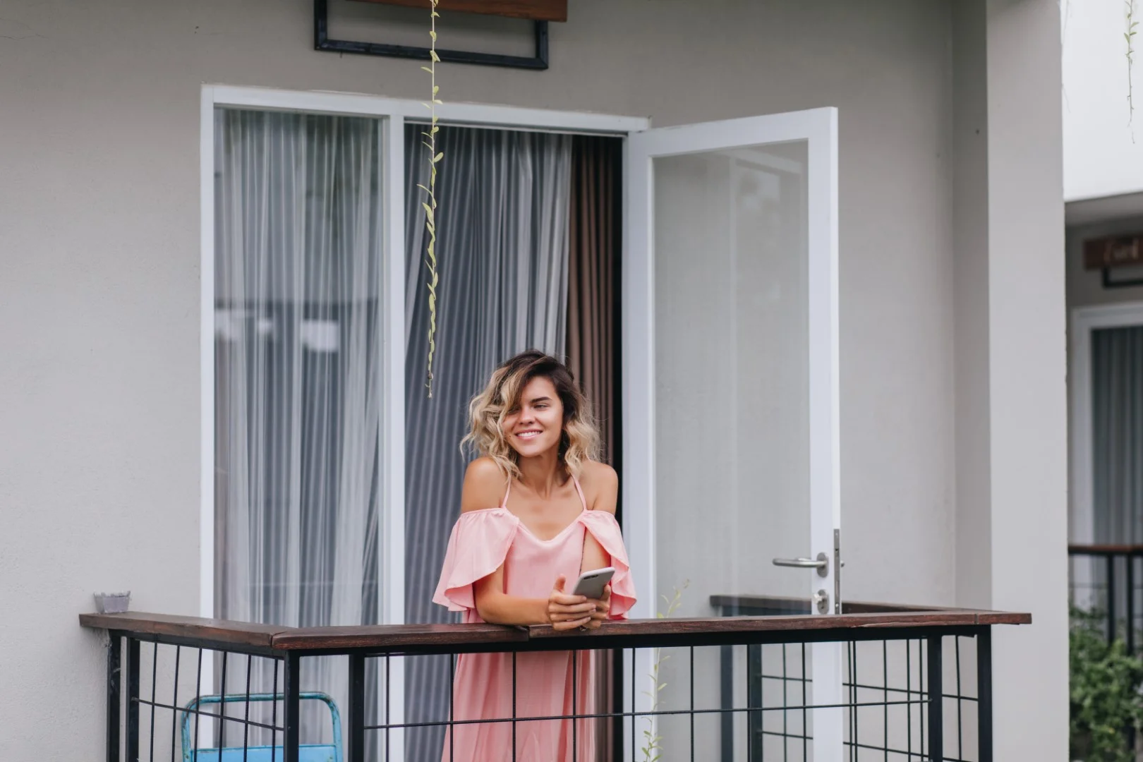 winsome tanned girl with phone hands smiling looking away cheerful young lady pink outfit standing hotel balcony Buyuk